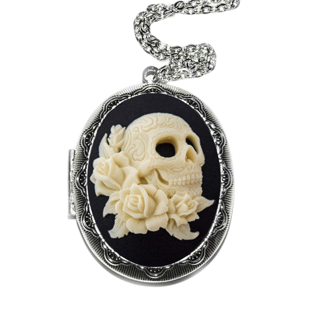 A silver locket with a carved white skull design and a floral arrangement on a black background.