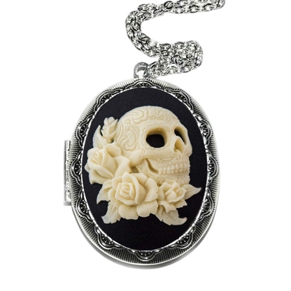 A silver locket with a carved white skull design and a floral arrangement on a black background.